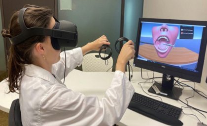 a person in white coat wears virtual reality glasses and holds handsets in front of a screen with an image of a mouth and teeth